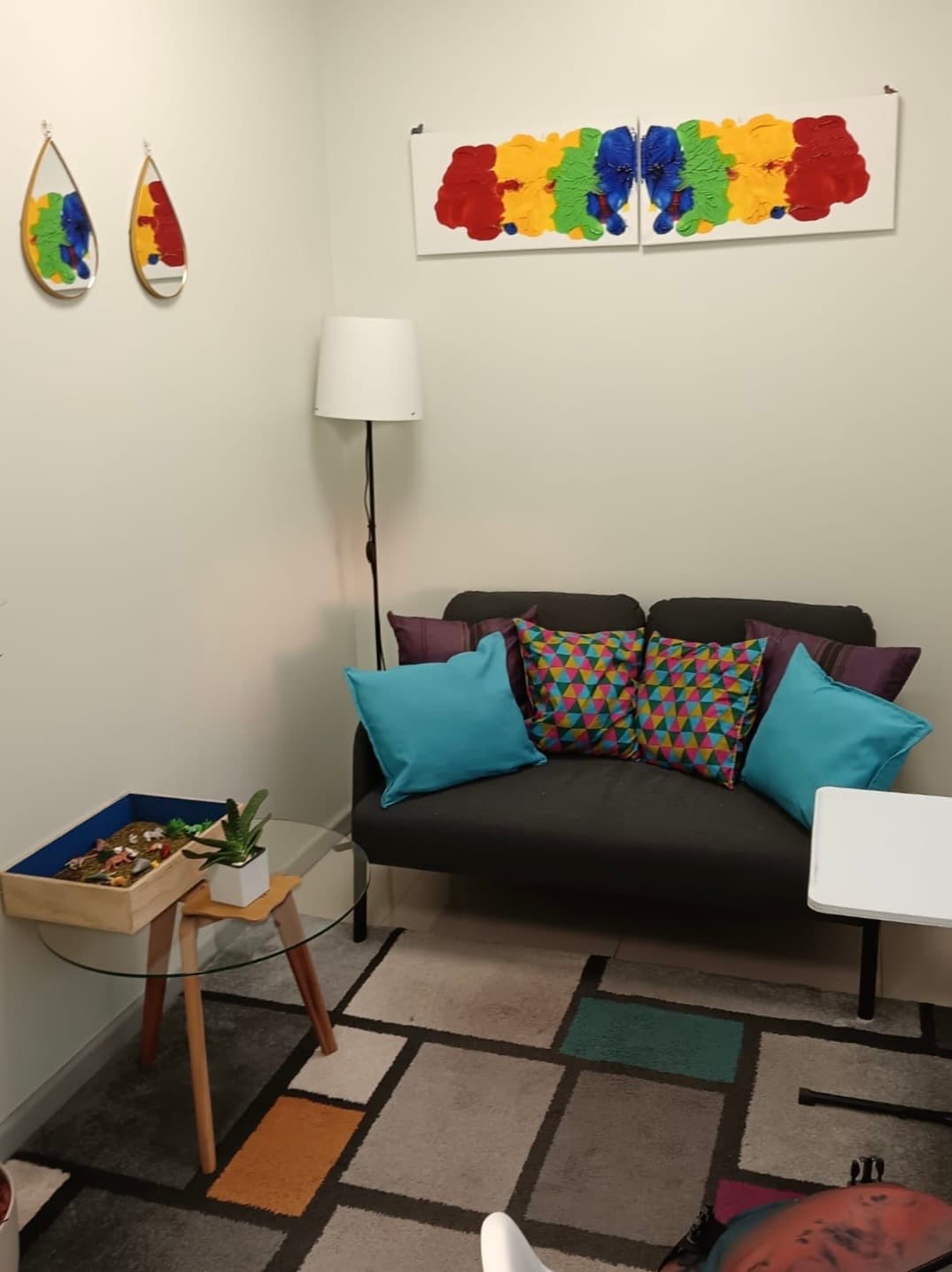 Sala acogedora con sofá, arte colorido y caja de arena para terapia de juego